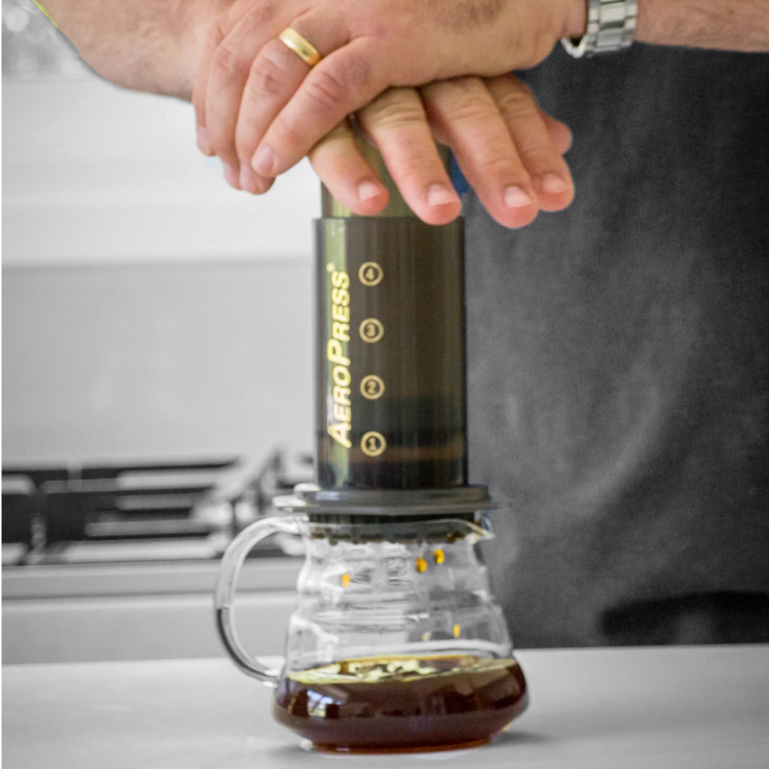 AeroPress coffee maker being pressed down to filter and brew the coffee. The coffee falls into the glass carafe. 