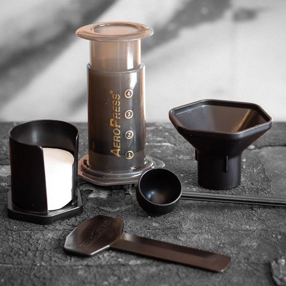 Photo of an Aeropress coffee maker alongside its filters, stirrer, scoop, and funnel. 