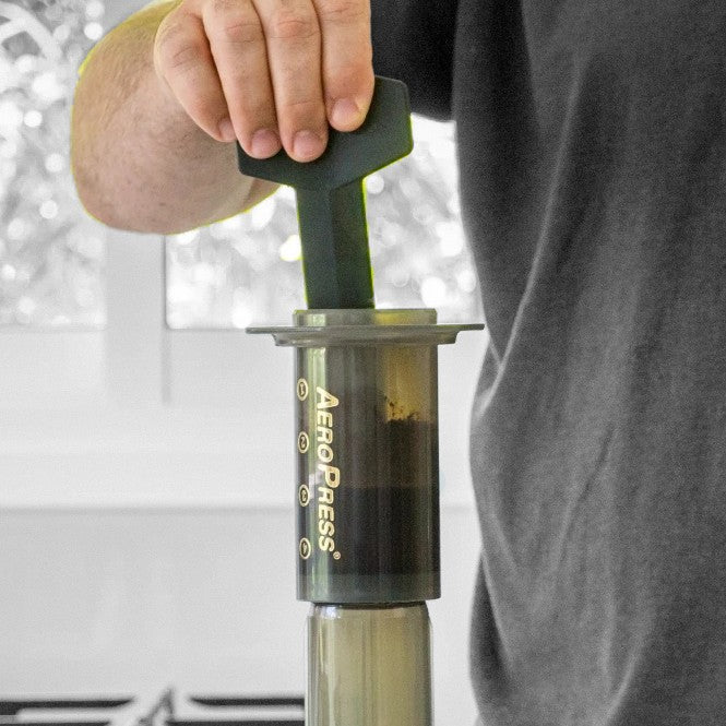 Image of an AeroPress with coffee brewing inside, being stirred by the Aeropress stirrer. 