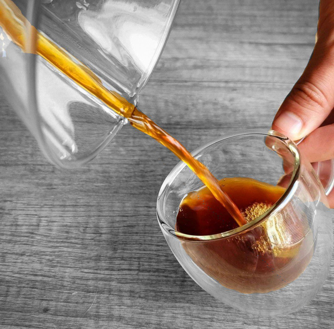 Coffee from a Chemex coffee maker being poured into a double walled glass coffee mug. 